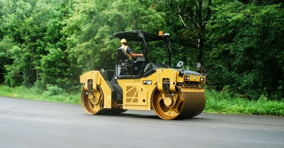 Man in a hard hat driving a Cat Compactor down the road