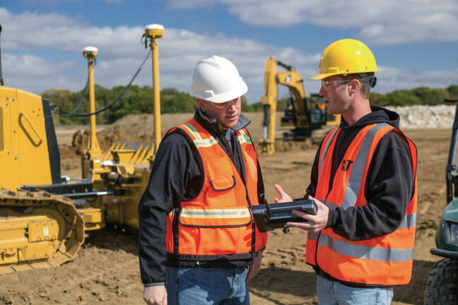 Two men on a construction site, looking at technology device