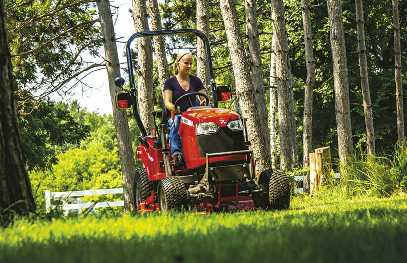 woman riding a red massy ferguson sub compact tractor in the yard