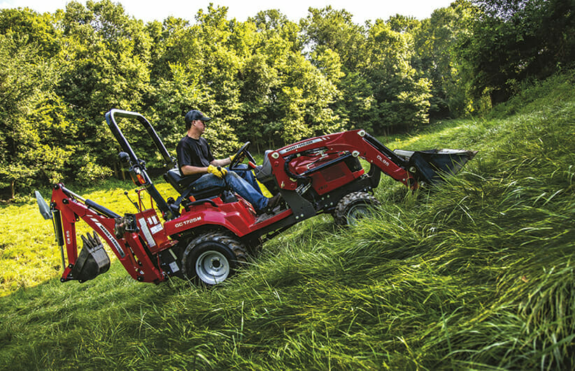 a man riding a red massy ferguson sub compact tractor up a grass hill