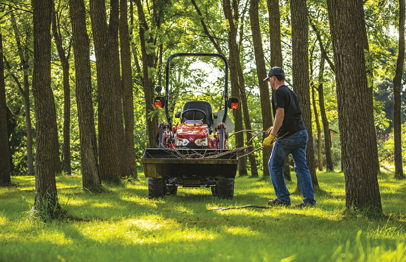 a man picking up sticks in the yard with a red massy ferguson sub compact tractor in the background