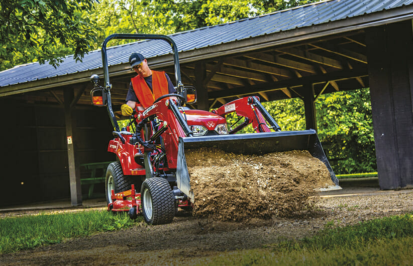 worker using a red massy ferguson sub compact tractor to dump dirt onto the ground